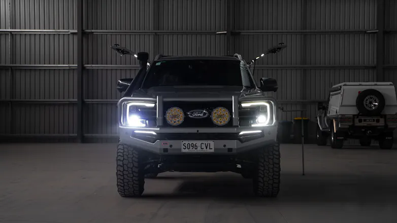 Silver Next-Gen Ford Ranger in darkened garage, with headlights turned on and canopy opened