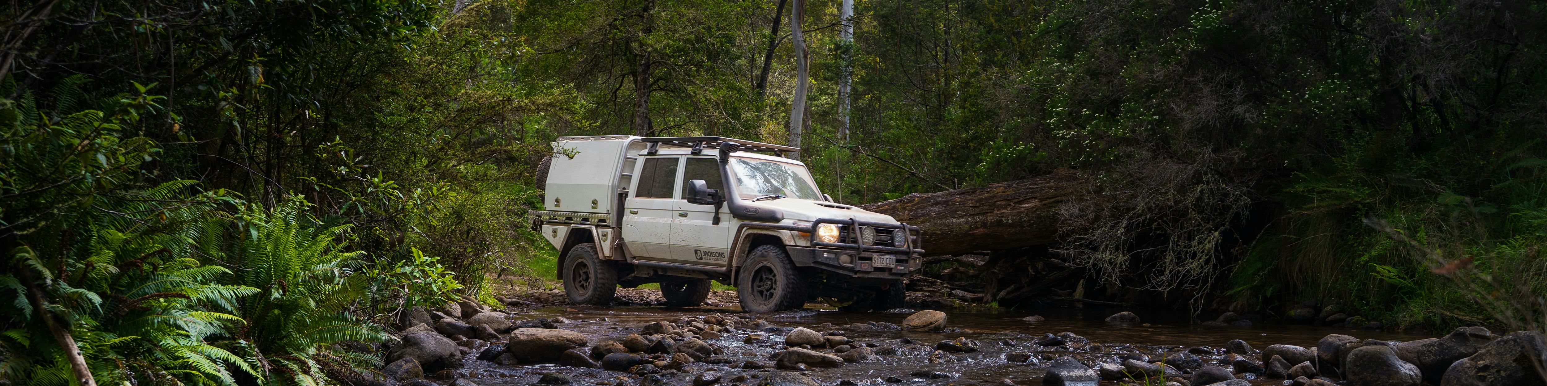 White 4x4 crossing a creek with modifications from Jacksons 4x4